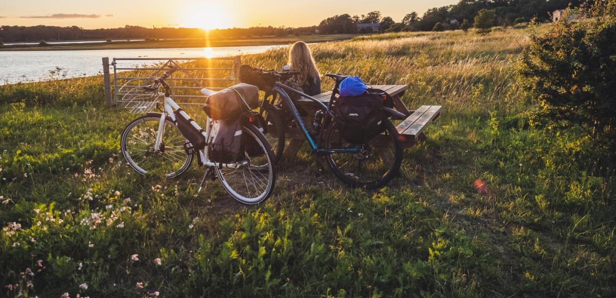 Kvinne slapper av ved et bord og en benk, midt på et jorde, og beundrer soloppgangen over vannet ved knudshoved på Fyn