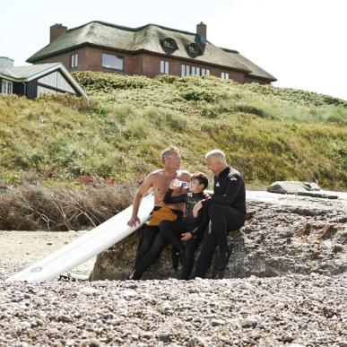 Two men and a child play on a beach beside a summerhouse in Denmark