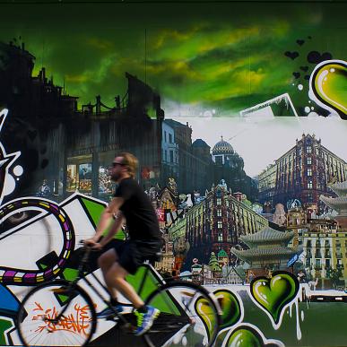A cyclist rides past a graffiti wall covered with green hearts