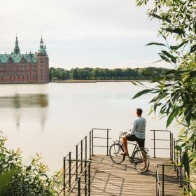 Cyclist stands looking at Frederiksborg Castle across the moat
